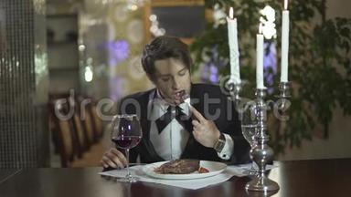 年轻男子穿着<strong>经典</strong>的燕尾服，切肉<strong>牛排</strong>，在餐厅享用晚餐
